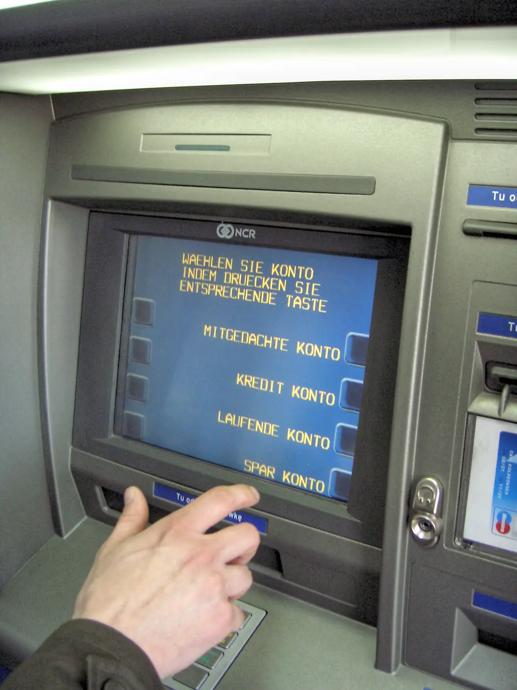A hand pressing a button on a bank ATM
